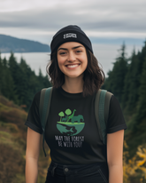 Person wearing a black t-shirt with a nature graphic and text, standing outdoors with trees and water in the background.